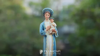 Góc nghiêng tượng Đức Mẹ La Vang cho thấy dáng áo dài, khăn xếp và phần cây đa phía sau